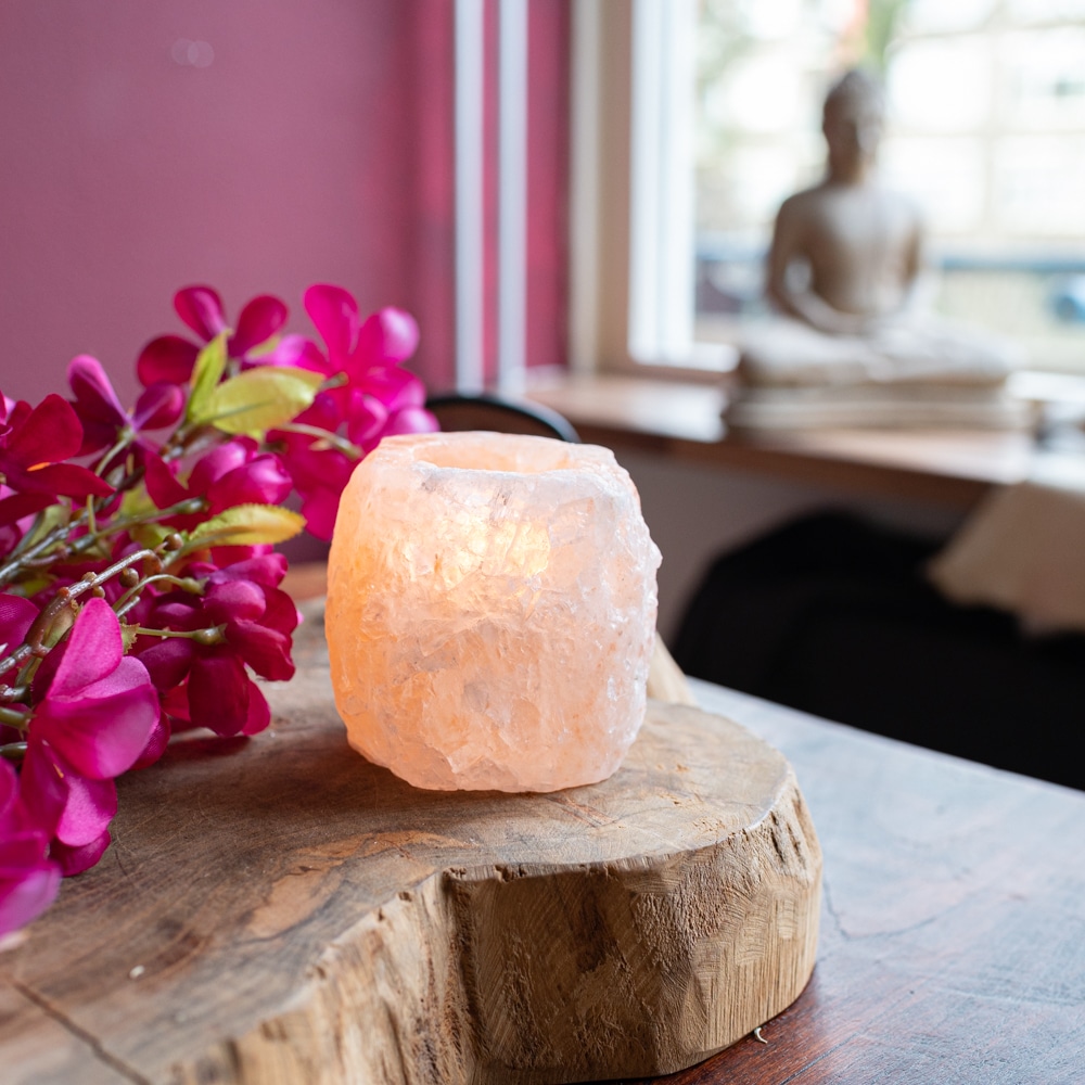 Salzlampe Salzteelichhalter auf Holzscheibe mit pinken Blumen Buddhastatue im Hintergrund