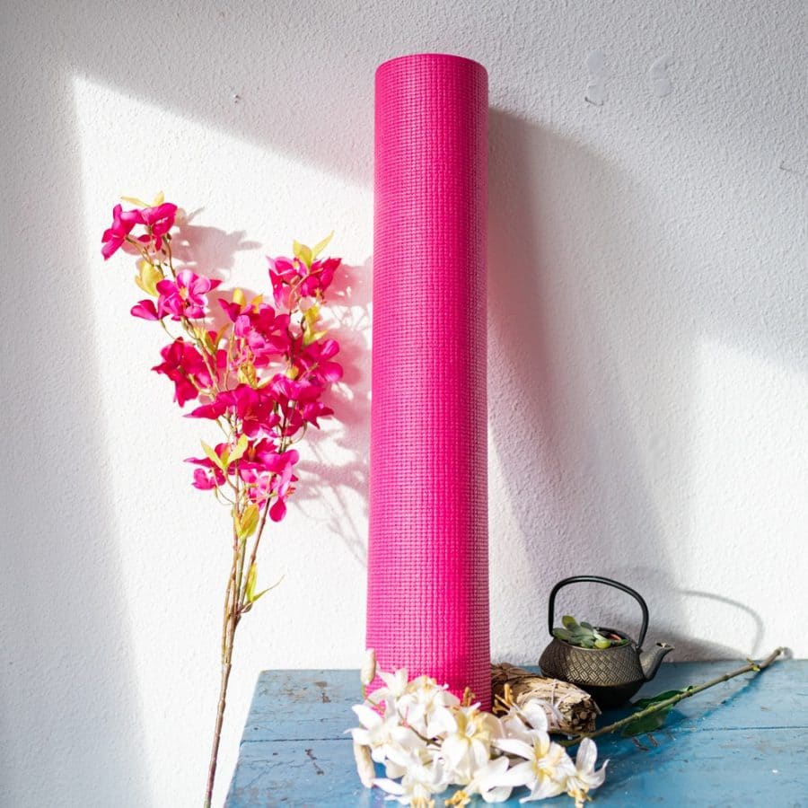 Pinke Yogamatte an weiße Wand gelehnt mit Blumen