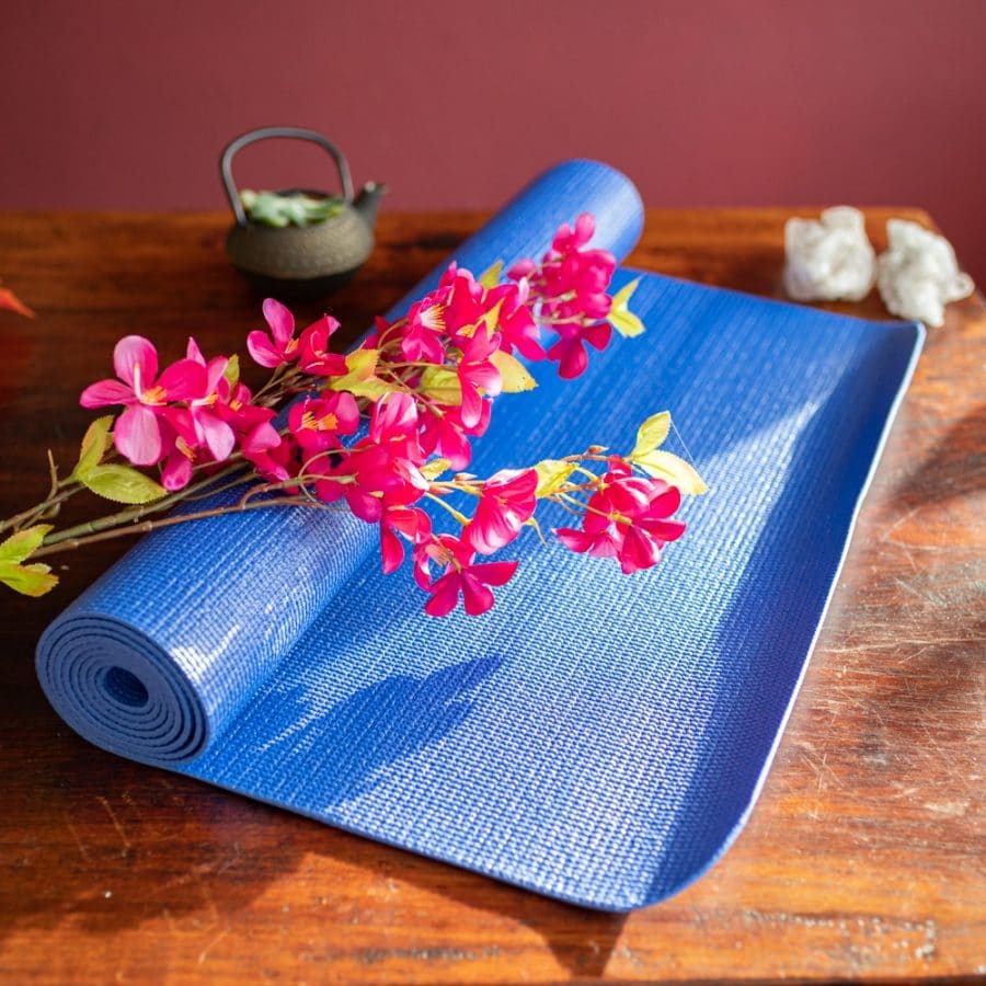 Blaue Yogamatte auf Holztisch vor roter Wand mit Blumen