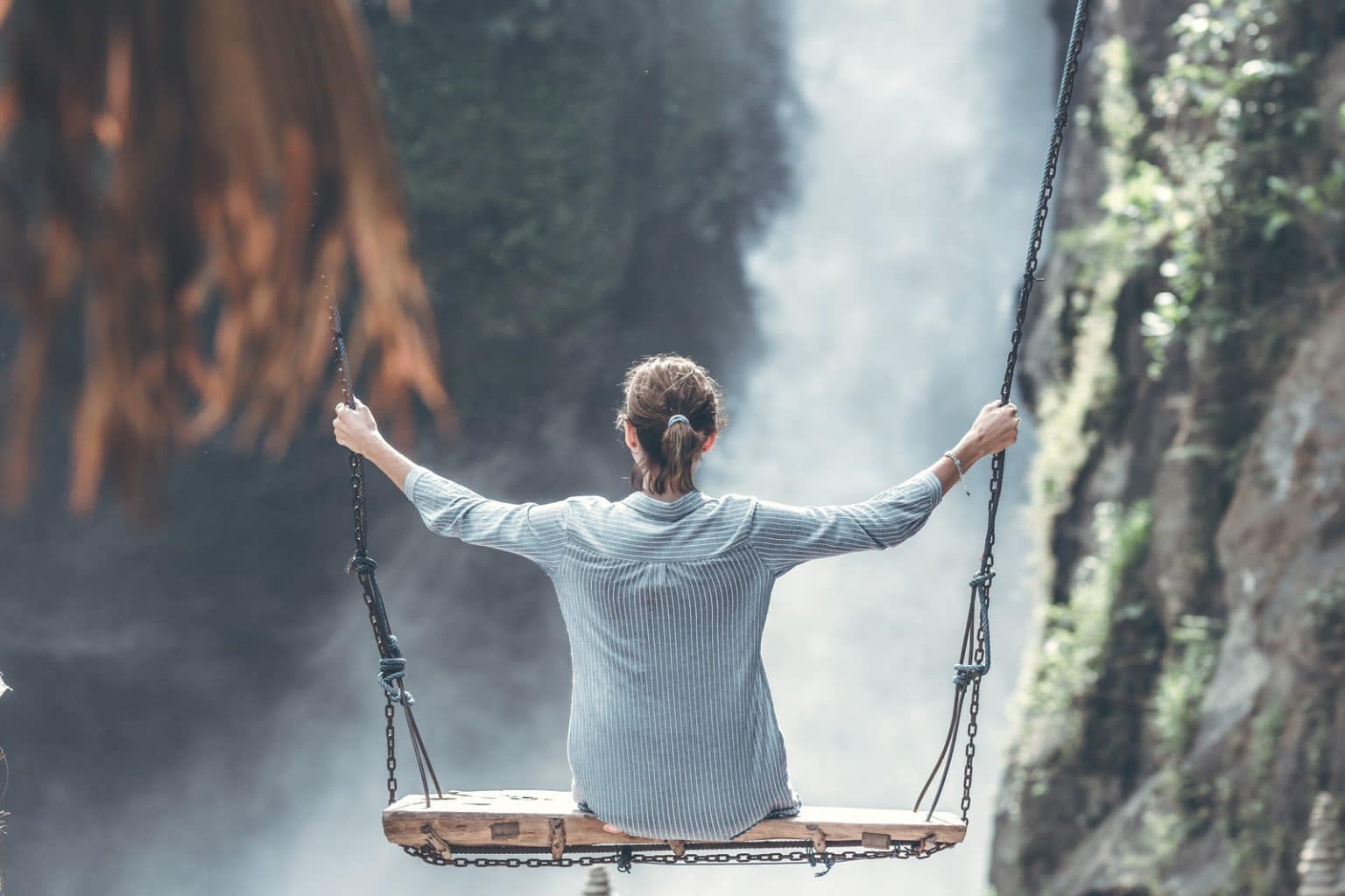 Frau mit gestreifter Bluse auf Schaukel vor Felsen und Wasserfall