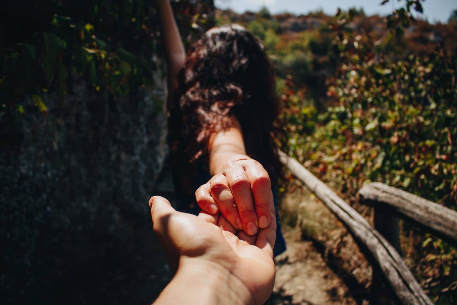 Frau läuft durch Natur in der Sonne und hält Hand im Vordergrund