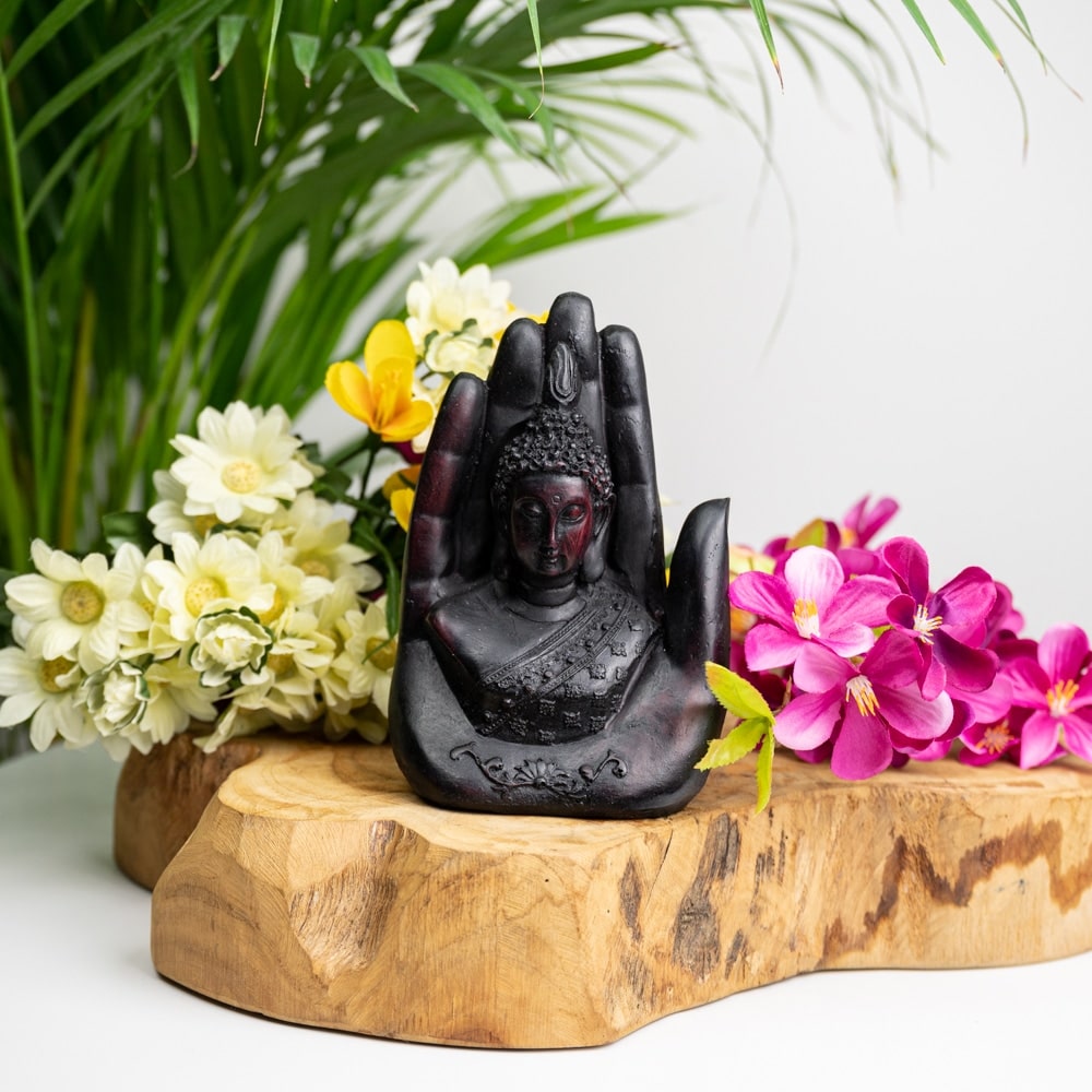 Buddha in Hand schwarz Statue auf Holzscheibe mit gelben und rosa Blumen