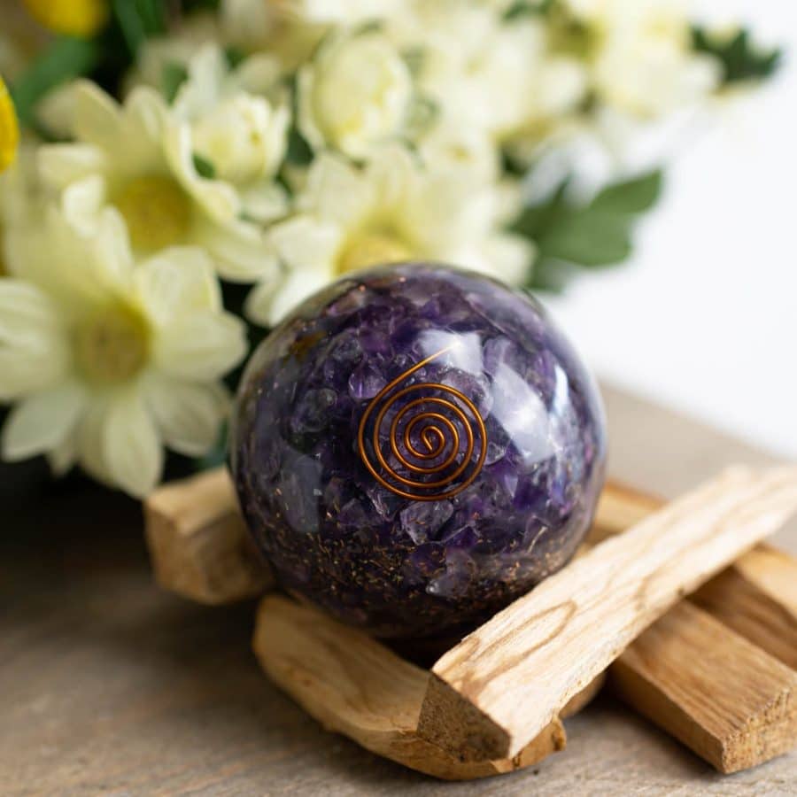 Orgonit kugel amethyst mit kupferspirale auf Holz mit blulmen
